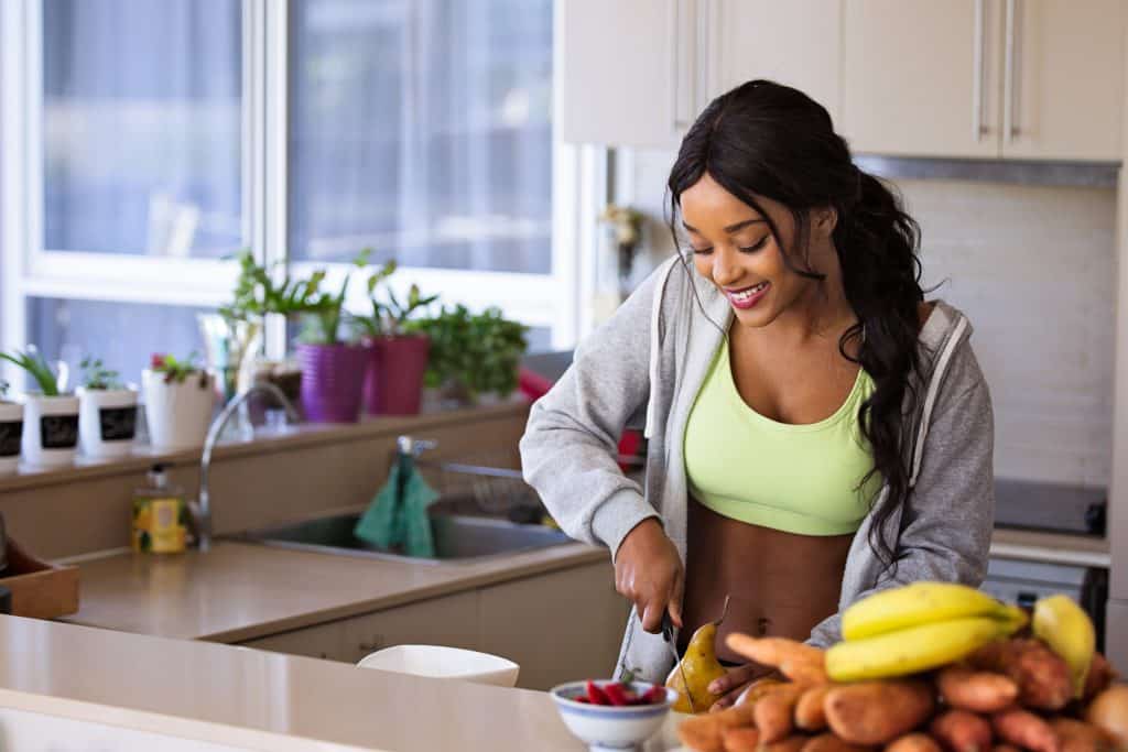 Mulher sorri enquanto corta frutas em sua cozinha.