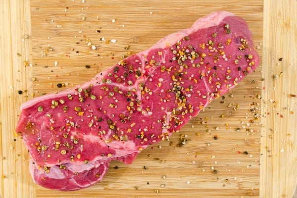 Pedaço de carne temperado visto de cima em tábua de madeira