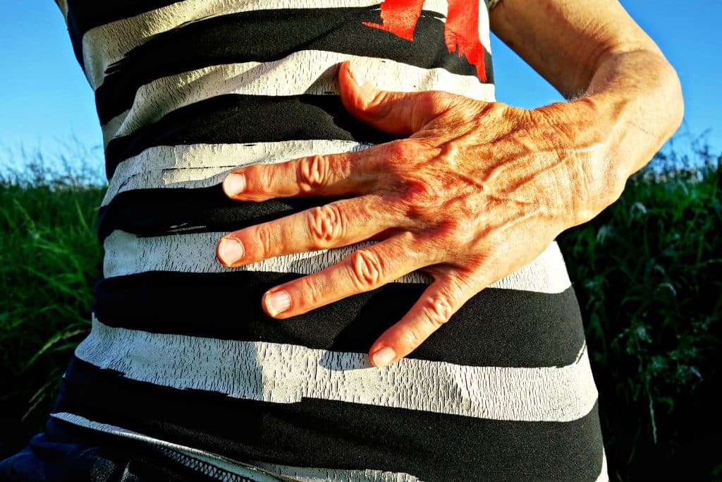 Imagem da silhueta de uma mulher do pescoço para baixo. Ela usa uma camiseta listrada nas cores preto e branco e está com uma das suas mãos sobre a região da barriga. Ela foi diagnosticada com o problema do útero bicorno.
