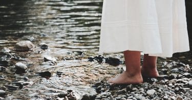 Mulher com seus pés descalços em pedras ao lado de um rio