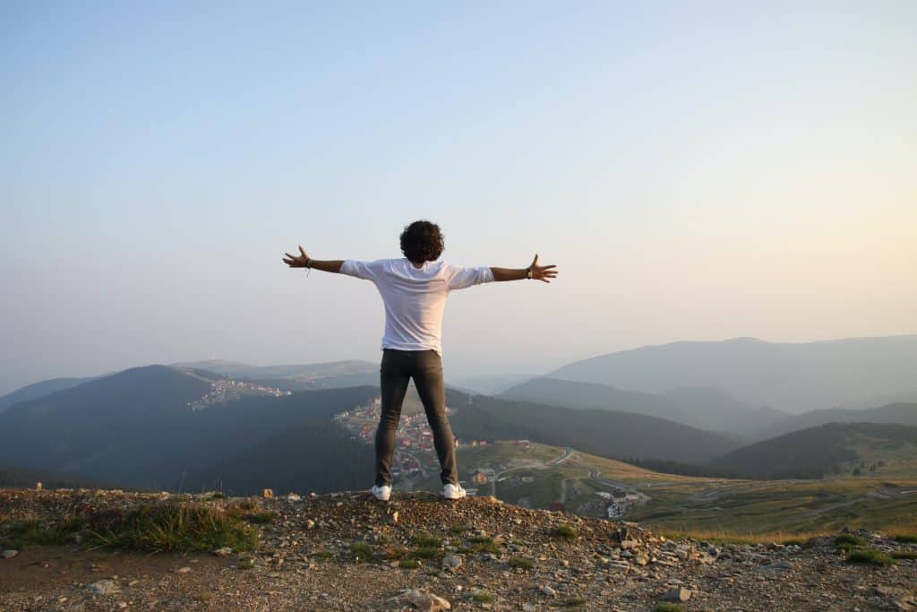 Homem em uma montanha olhando para o horizonte com os braços abertos