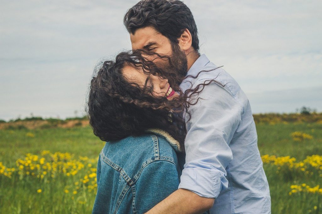 Casal abraçado com homem beijando rosto de mulher e campo ao fundo