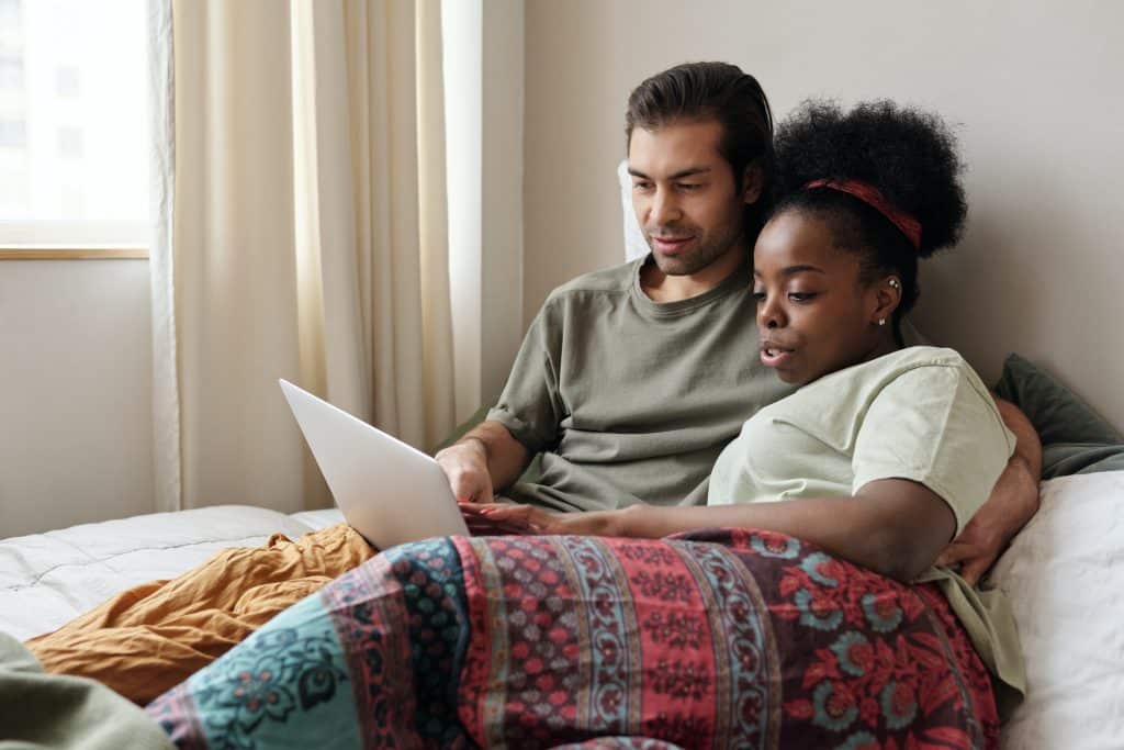 Foto de um homem e uma mulher deitados no sofá, abraçados, usando o computador.