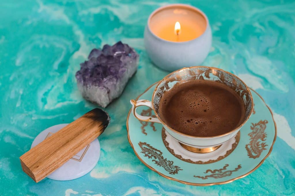 Uma xícara de chá, uma vela, um cristal e um incenso de madeira sobre uma mesa