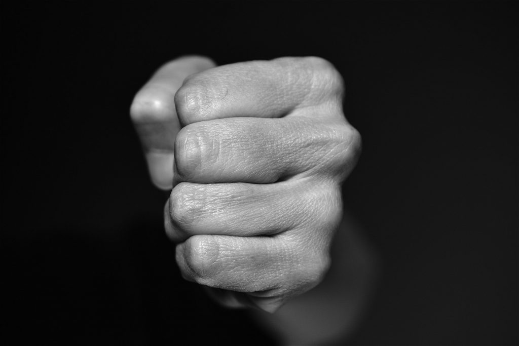 Imagem em preto e branco da mão fechada de um homem pronto para agredir.