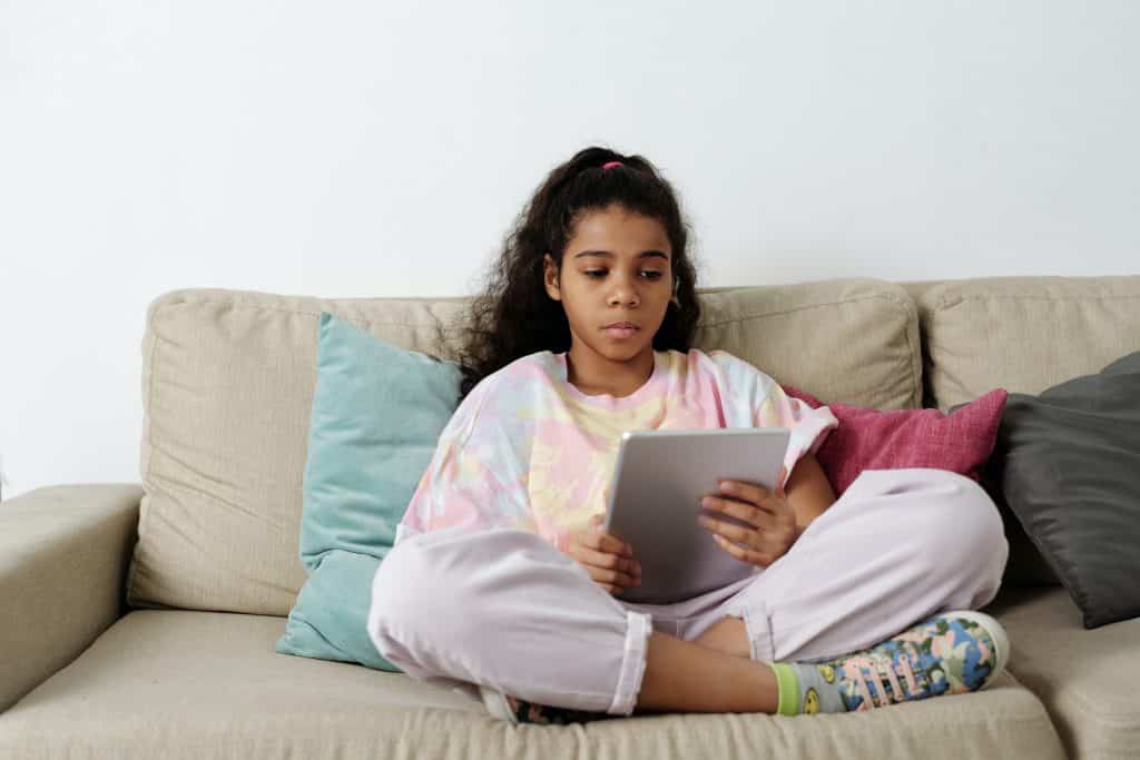 Menina sentada no sofá usando seu tablet.