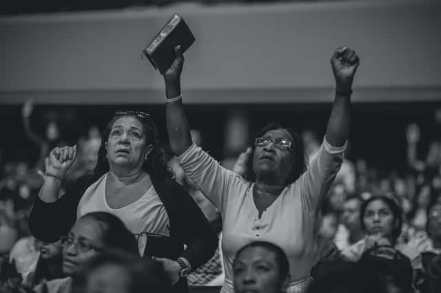 Mulheres em pé em culto com braços para o alto e bíblia na mas mãos