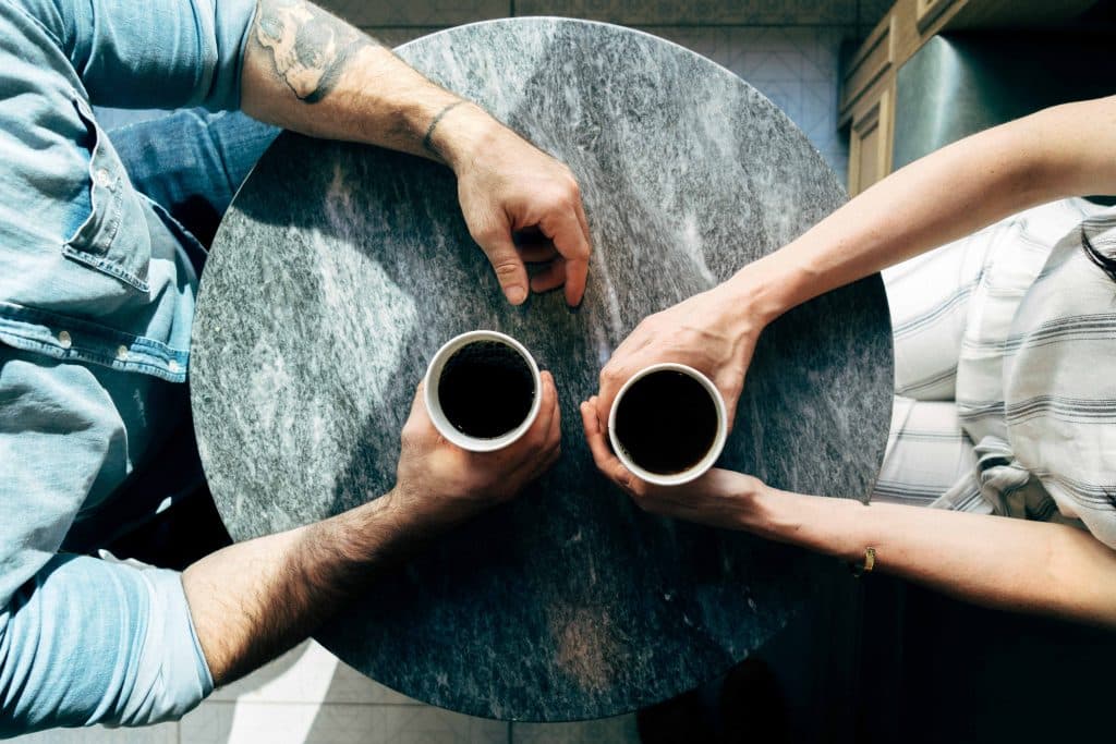 Duas pessoas conversando sentadas segurando xícara de café