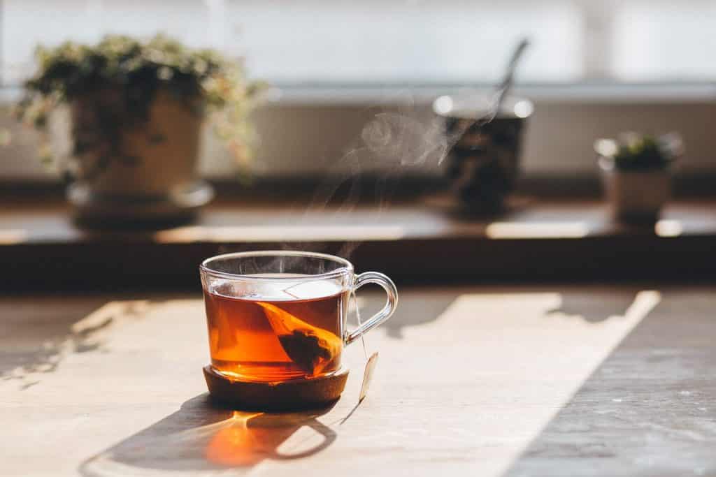 Imagem de chá para dor de estômago e fígado em infusão e servido em uma xícara de vidro.