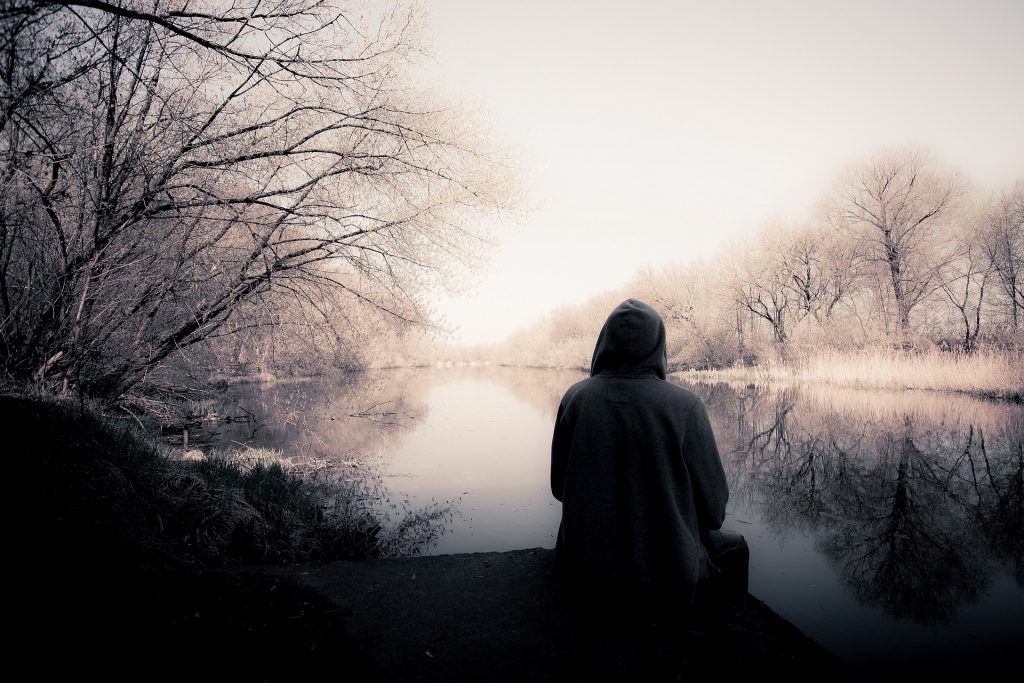 Imagem de homem solitário e ansioso. Ele está sentando em um pier olhando para um lago.
