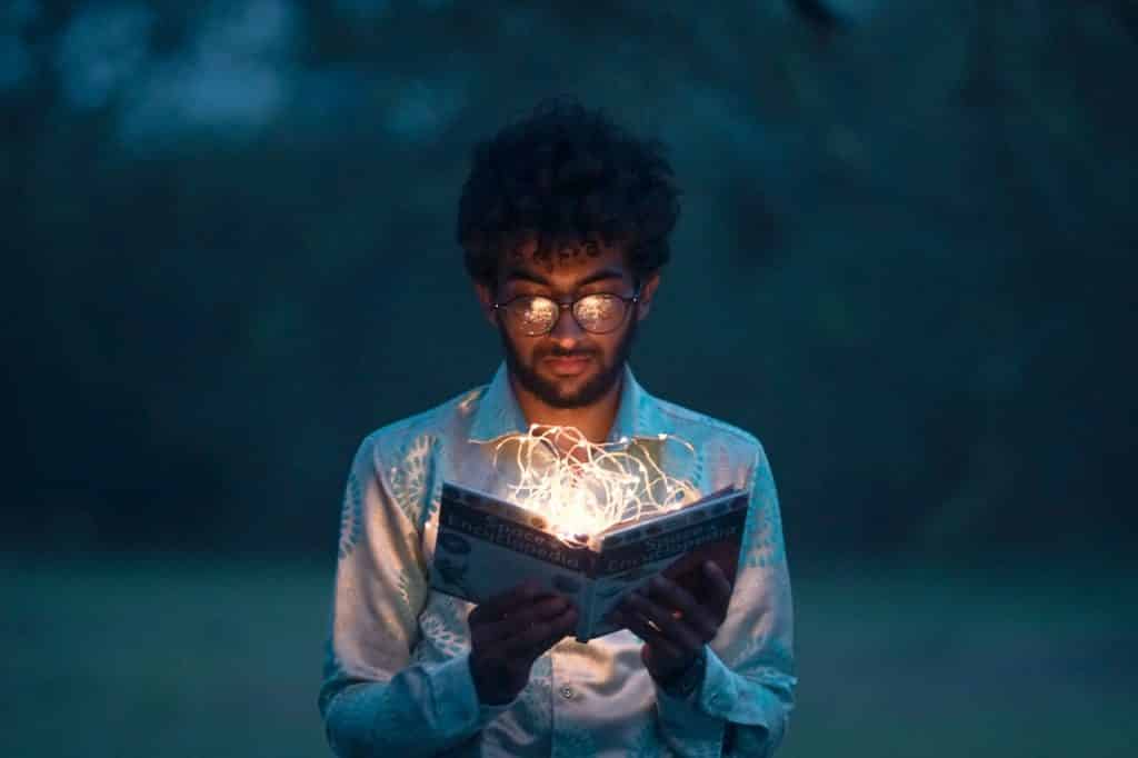 Homem com livro aberto, e dentro dele, várias luzes estão acesas.