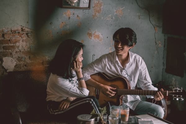 Casal em sala de casa com homem tocando violão e mulher cantando