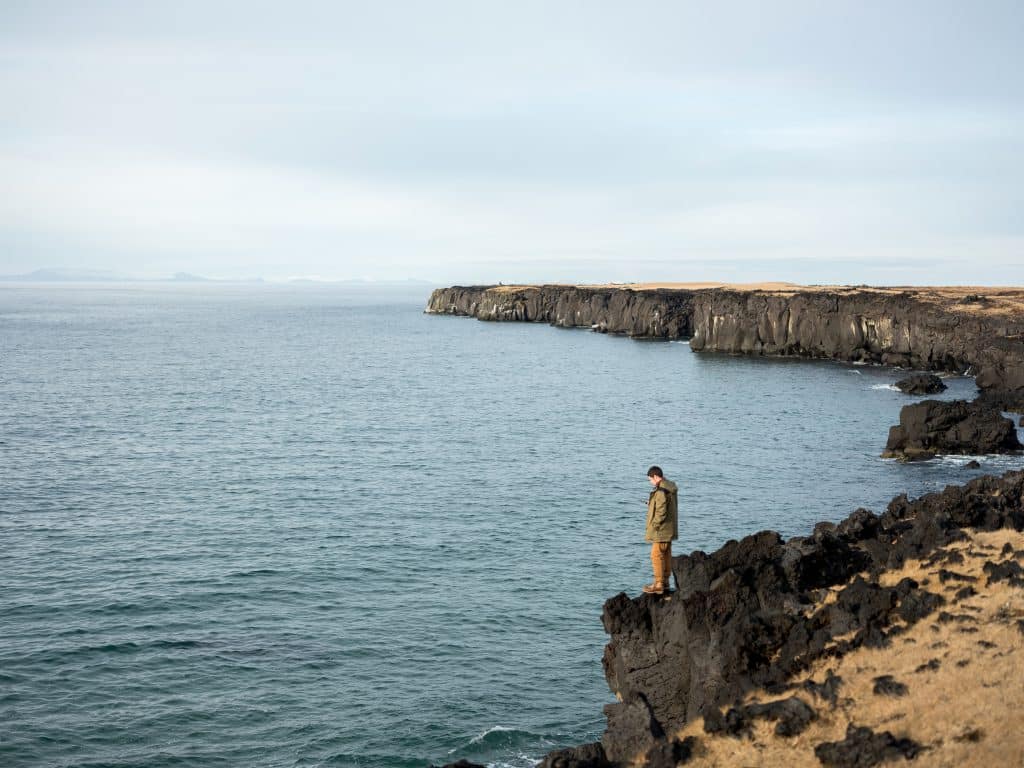 Homem em pé sobre uma rocha, em frente ao mar.