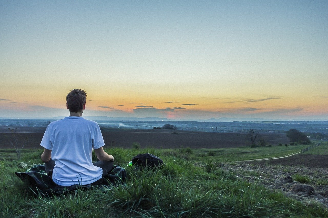 Homem sentado em campo gramado, meditando.