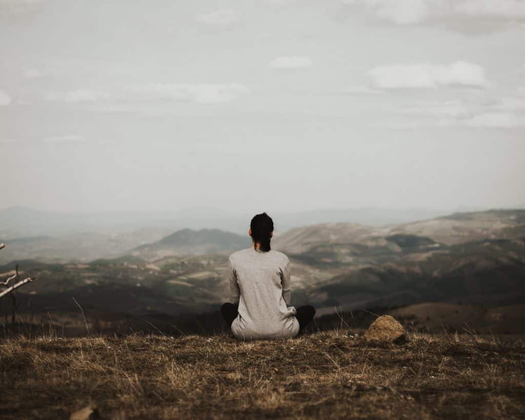 Mulher sentada em uma montanha olhando para o horizonte