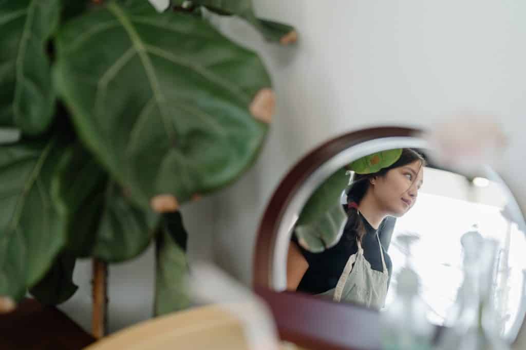 Reflexo de uma mulher vista de perfil em um espelho, com plantas ao lado.