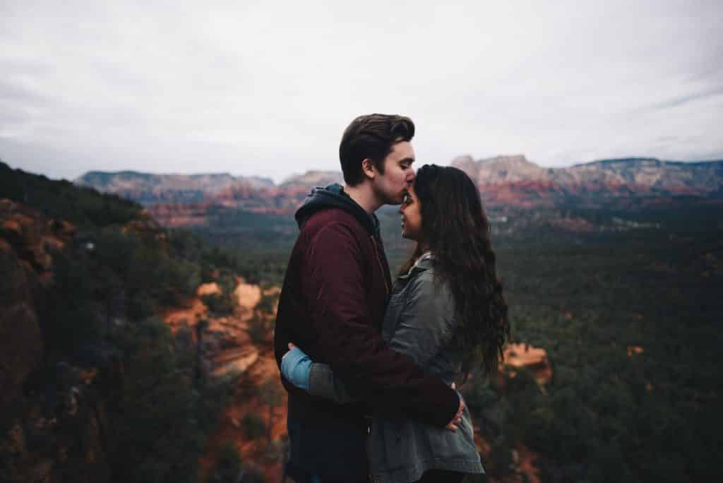 Homem beijando testa da mulher a sua frente em uma  montanha