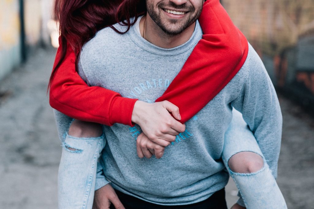 Imagem de um casal jovem. Ele carrega a moça em suas costas. Estão felizes. A imagem retrata a questão da relação entre o casal e o orgasmo feminino.