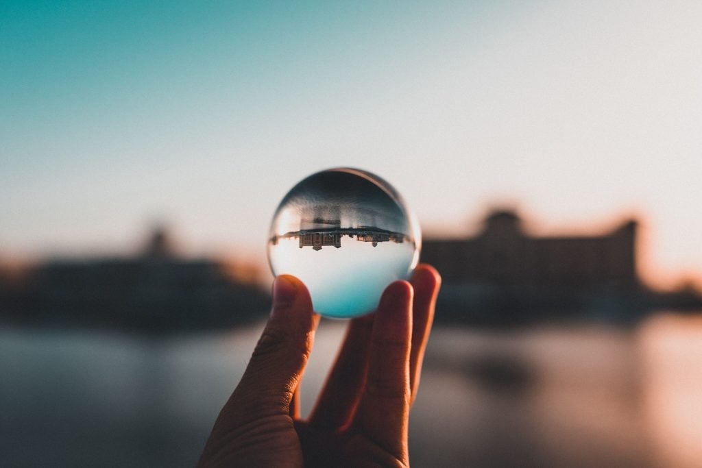 Pessoa segurando um pequeno globo de vidro em frente a uma paisagem com um rio em um dia ensolarado.