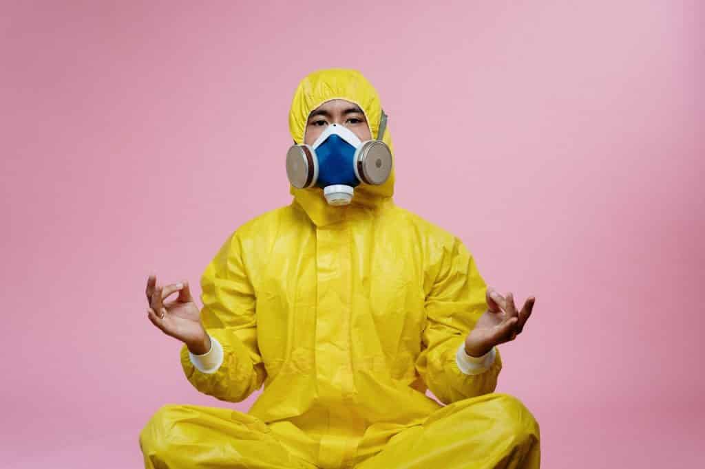 Homem com roupa e máscara de isolamento, sentado com as pernas cruzadas, meditando.