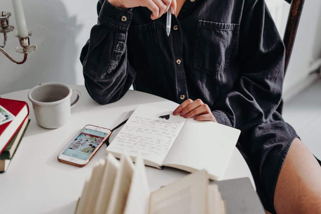 Mulher sentada em uma mesa, lendo notas em um caderno enquanto toma café.