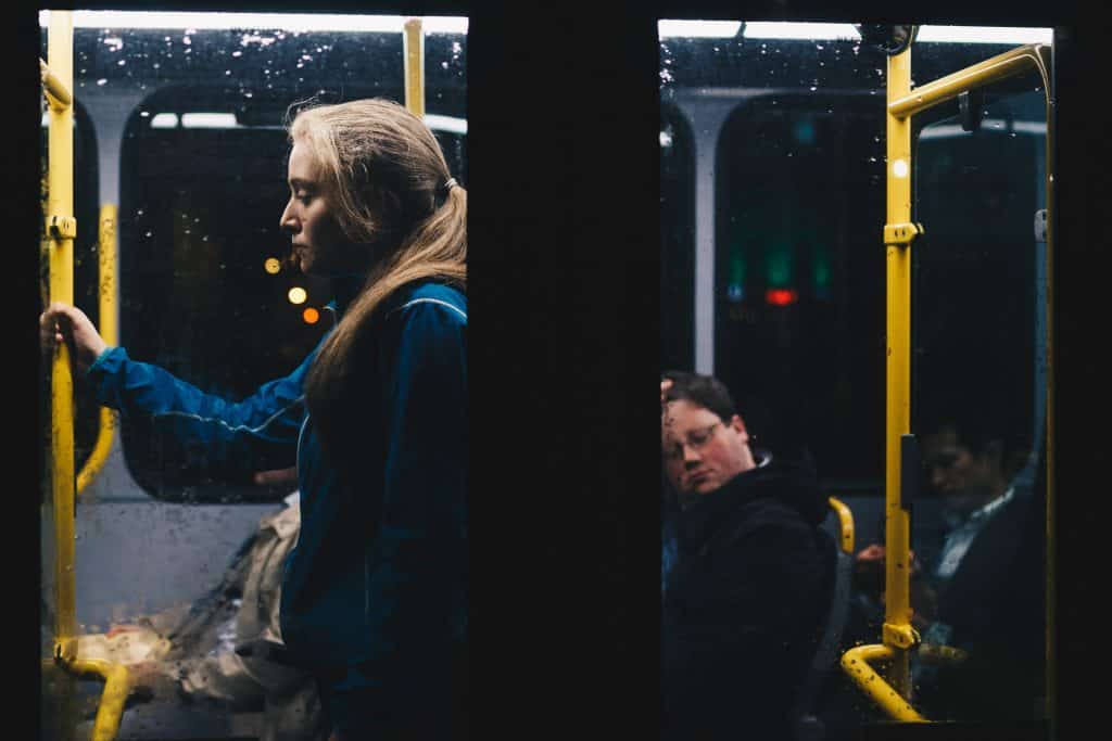 Mulher em pé vista da janela de um ônibus à noite.