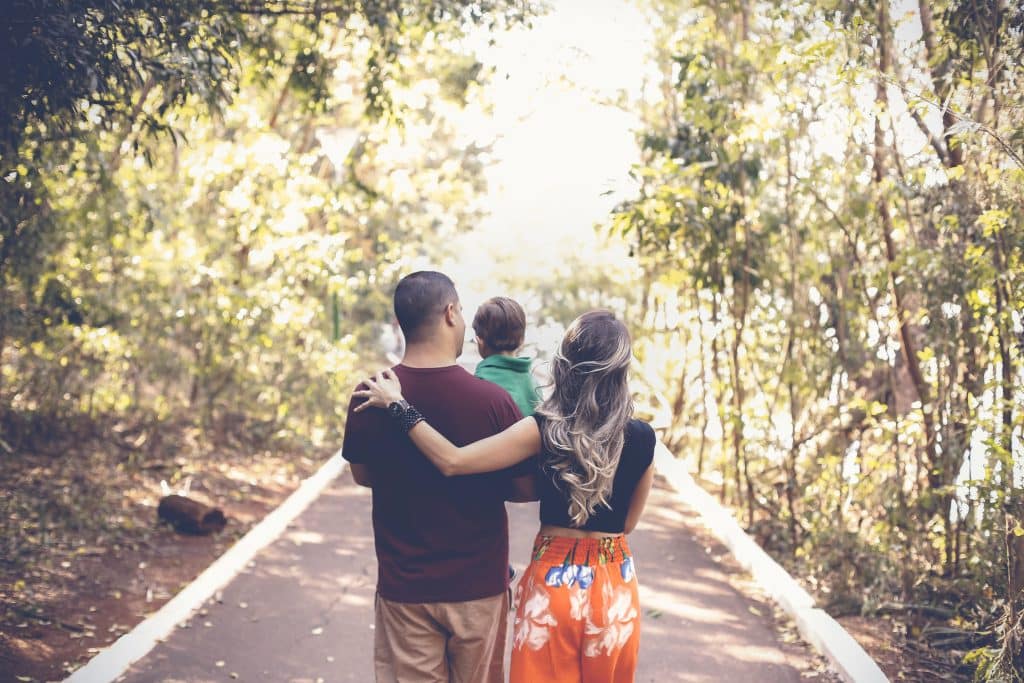 Mãe, pai e criança caminhando por um parque, vistos de costas.