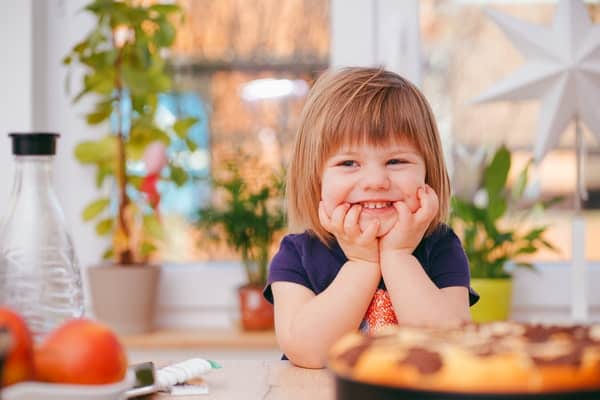 Menina com braços apoiados na mesa e mãos no rosto sorrindo