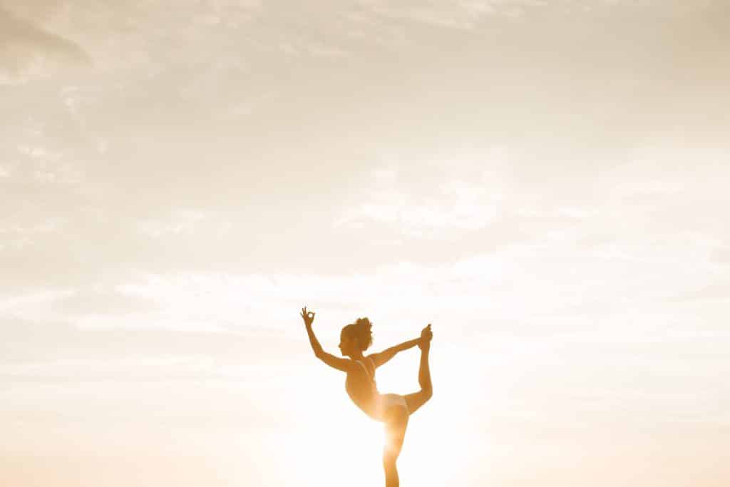 Mulher praticando Yoga ao ar livre, ao pôr do sol.