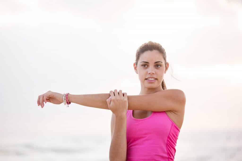 Mulher com roupas de ginástica alongando os braços.