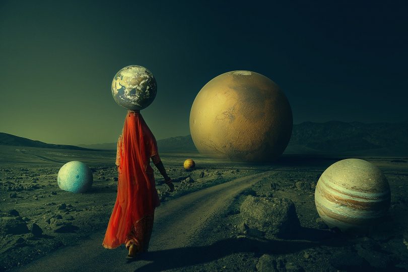 Imagem de uma mulher caminhando e segurando sobre a cabeça um planeta. Ao fundo da imagem e ao lado, vários planetas. A imagem retrata a transição planetária.