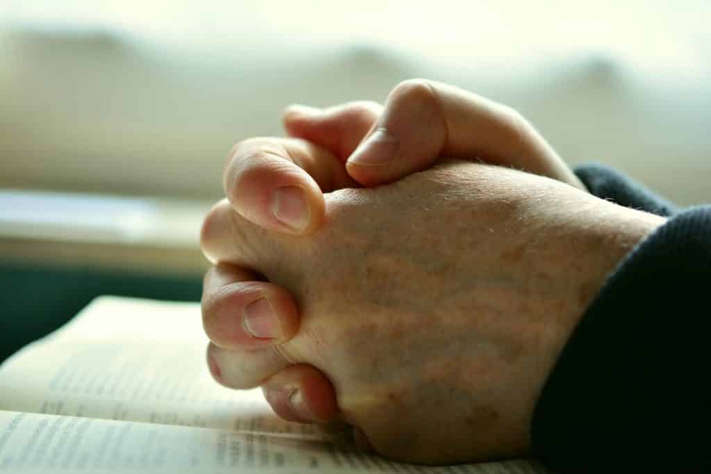 Imagem de mãos juntas em sinal de oração. As mãos estão sobre a bíblia em sinal da oração do perdão.