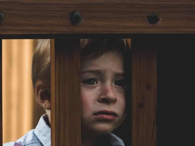Garoto com expressão triste atrás de cerca de madeira