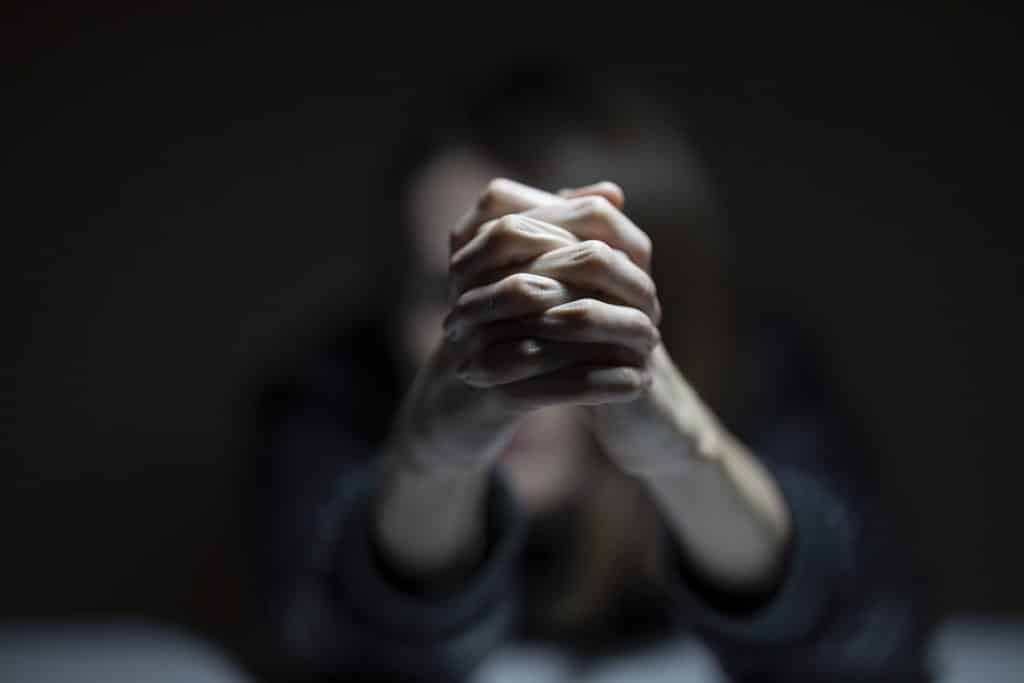 Imagem da silhueta de uma mulher que está sentada, com os braços esticados e com as mãos dadas. Ela parece estar triste e depressiva.