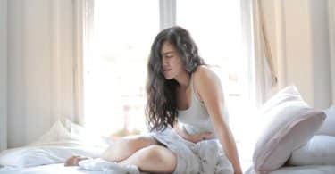 Mulher sentada na cama com dor na barriga
