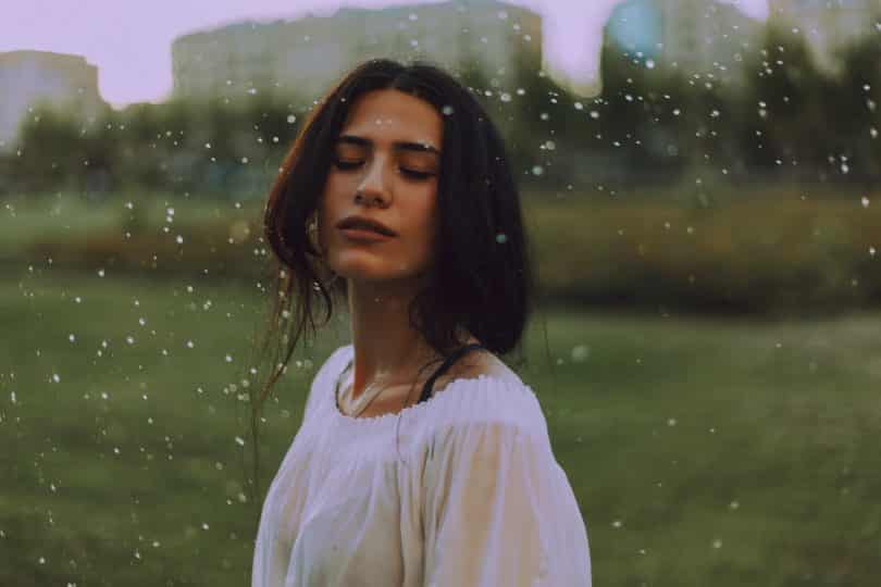 Mulher de olhos fechados em ambiente aberto, sob a chuva.