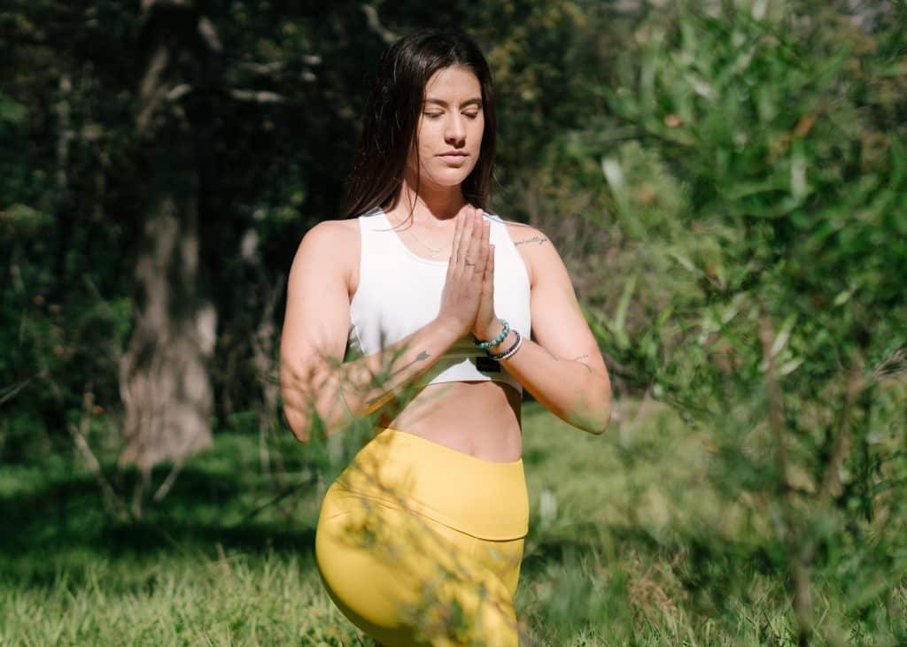 Mulher em pé, com roupas de ginástica, rezando em um parque.