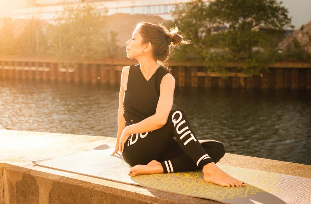 Mulher praticando yoga ao ar livre, ao lado de um rio.