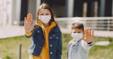 Crianças com máscara e mãos em frente ao corpo