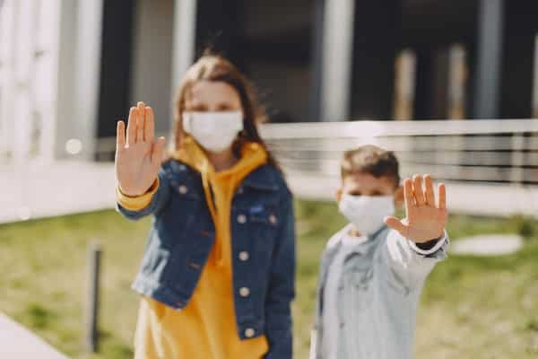 Crianças com máscara e mãos em frente ao corpo