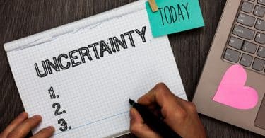 Caderno com a palavra "uncertainty" e notebook ao lado.