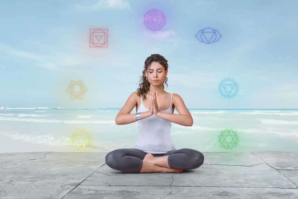 Mulher sentada em posição de lótus com desenhos dos chakras em volta dela.