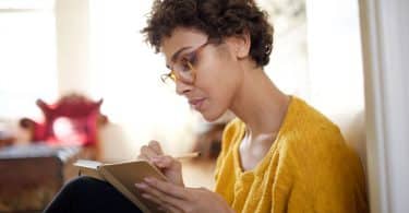 Mulher sentada escrevendo em caderno concentrada