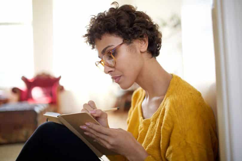 Mulher sentada escrevendo em caderno concentrada