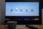Televisão mostrando a animação da Pixar e na mesa em frente uma xícara e um controle da TV