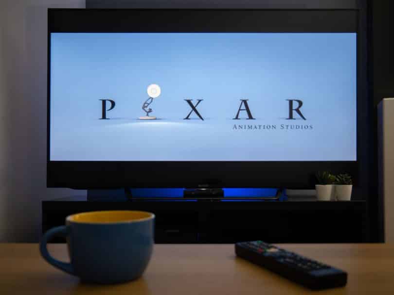 Televisão mostrando a animação da Pixar e na mesa em frente uma xícara e um controle da TV