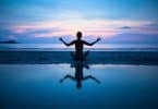 Mulher sentada meditando na praia com céu rosa e azul ao fundo