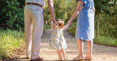 Avô e avó andando de mãos dadas com sua neta pequena, que olha para trás.