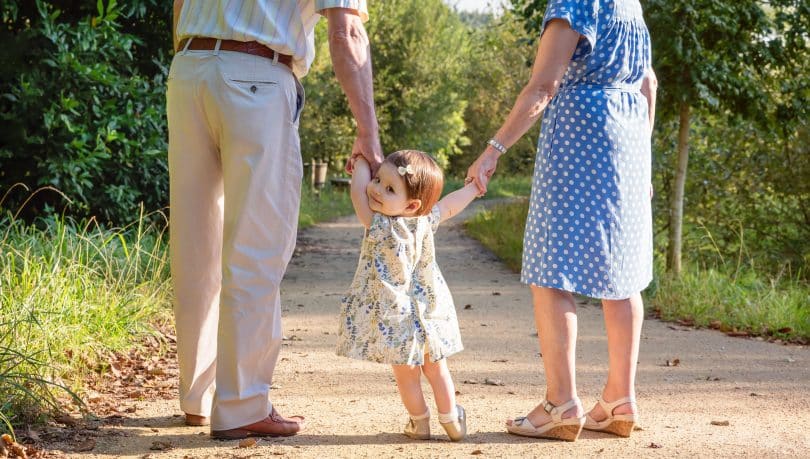 Avô e avó andando de mãos dadas com sua neta pequena, que olha para trás.