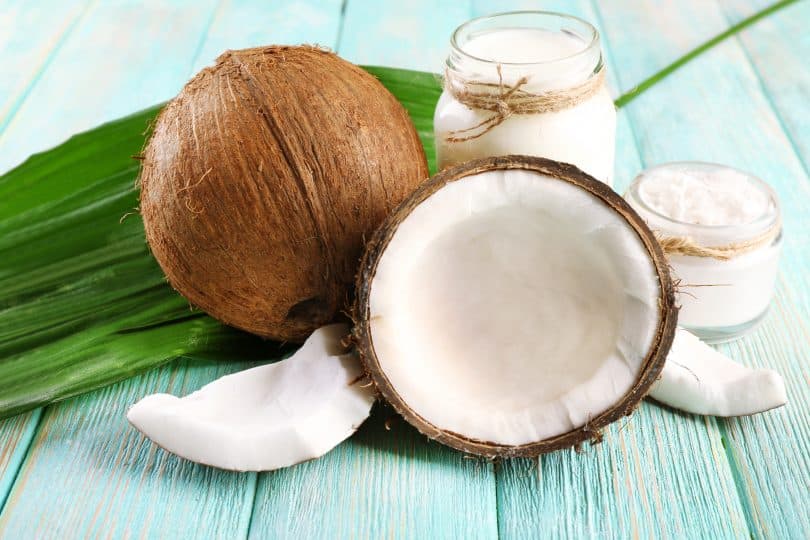 Imagem de metade de um coco e um coco inteiro sobre uma mesa de madeira pintada de azul claro.